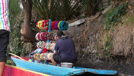 Vista-De-Un-Vendedor-Con-Sombreros-Florales-Coloridos-En-Un-Barco-Para-Vender-A-Los-Turistas-A-Lo-Largo-De-Los-Canales-De-Xochimilco