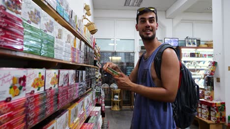 Turista-Masculino-Con-Mochila-Dentro-De-La-Tienda-Recogiendo-Una-Caja-De-Delicias-Turcas-Del-Estante