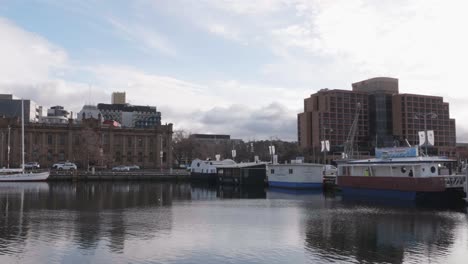 Best-view-of-Hobart-waterfront-with-traffic-driving-on-street-and-Grand-Chancellor-Hotel-in-background,-Constitution-Dock-surrounded-by-fish-punts-on-clear-winter-day,-Tasmania,-Australia