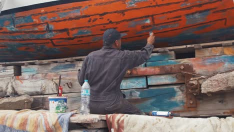 Greek-fisherman-repairs-wooden-fishing-boat-with-waterproof-caulking-slow-motion-wide-shot
