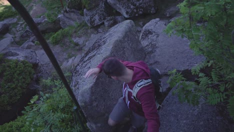 Young-tourist-man-is-climbing-down-a-ladder-from-top-of-rock,-low-angle-shot