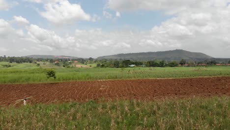 Toma-Aérea-De-Un-Hombre-Que-Lleva-Madera-En-La-Cabeza-Entre-Campos-Agrícolas-En-África-Rural