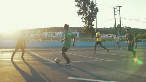 Grupo-De-Niños-Y-Hombres-Refugiados-Jugando-Al-Fútbol-En-Una-Cancha-Asfaltada