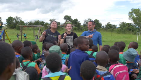 Ein-Paar-Amerikaner-Singen-Und-Tanzen-Für-Eine-Menge-Afrikanischer-Kinder,-Die-Draußen-In-Einer-Ländlichen-Gegend-Mitsingen-Und-Tanzen,-Zeitlupe-Im-Weitwinkel