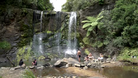 Gruppe-Junger-Menschen-Sitzen-An-Den-Mokora-Falls,-Auckland,-Neuseeland