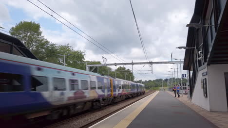 Toma-Panorámica-De-Un-Tren-Del-Norte-Que-Pasa-Por-Una-Estación-De-Cercanías-En-Las-Afueras-De-Leeds-En-Cámara-Lenta