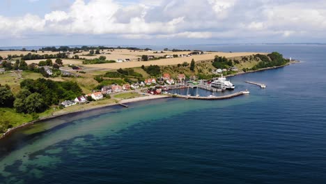 Vista-Aérea-Acercándose-Y-Bajando-Hacia-El-Pueblo-Y-El-Puerto-De-Bäckviken-En-La-Isla-De-Ven-En-El-Sur-De-Suecia-Durante-Un-Cálido-Día-De-Verano