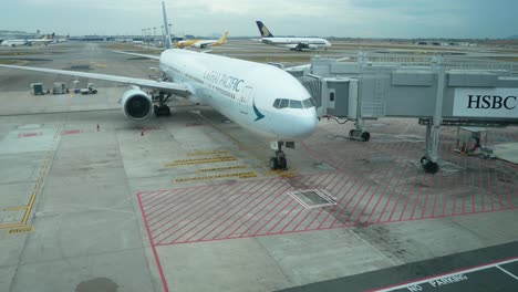 Vista-Panorámica-Desde-El-Interior-Del-Aeropuerto-De-Singapur-Con-El-Estacionamiento-Del-Avión-Cathay-Pacific-En-La-Puerta-Y-Algunos-Aviones-Se-Mueven-En-El-Fondo