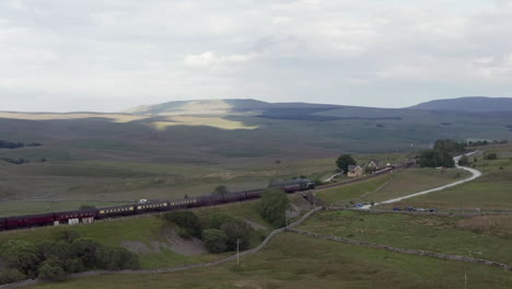 Toma-Aérea-Del-Tren-De-Vapor-Flying-Scotsman-60103-Que-Pasa-Por-La-Estación-Ribblehead-En-North-Yorkshire-Con-Un-Cultivo-Estrecho