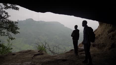 La-Silueta-De-Dos-Hombres-Africanos-Y-Un-Perro-Dentro-De-Una-Cueva-Mientras-Miran-Hacia-Un-Valle-Africano