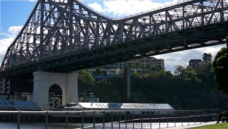 Corredores-Corriendo-A-Lo-Largo-De-La-Orilla-Del-Río-Brisbane-Iluminado-Por-El-Sol-En-Kangaroo-Point,-Con-El-Icónico-Puente-De-La-Historia-Elevándose-En-Lo-Alto