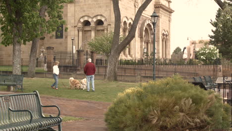 Una-Pareja-De-Jubilados-Pasea-A-Sus-Perros-En-El-Patio-Junto-A-Una-Antigua-Iglesia-Todavía-Baleada