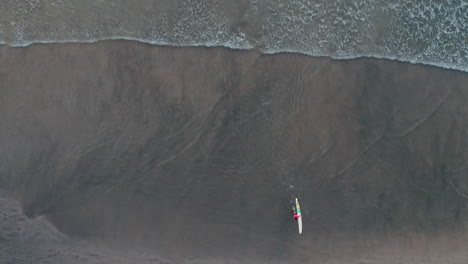 Toma-Aérea-De-Un-Surfista-Solitario-Saliendo-Del-Océano-En-Una-Playa-Desierta-En-Tambor,-Costa-Rica-4k-Cámara-De-Arriba-Hacia-Abajo-Bajando-Rápido