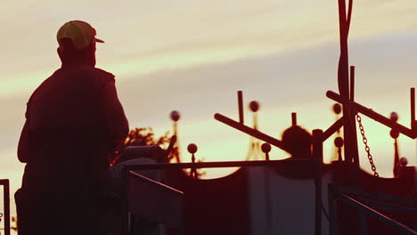 Carnival-worker-watching-ride-spin-at-sunset,-Close-Up