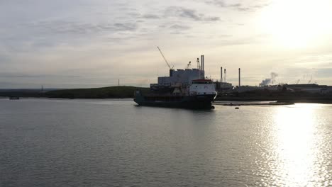 Low-aerial-shot-drifting-past-a-loading-ship-on-the-Swale-Estuary-in-Kent,-UK-to-reveal-a-power-station-and-industry-on-the-river-bank