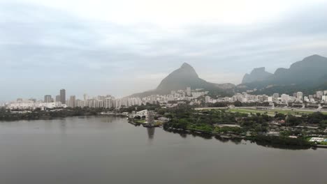 Panorámica-Aérea-Alrededor-Del-Lago-De-La-Ciudad-Con-Un-árbol-De-Navidad-Flotante-Parcialmente-Construido-En-La-Orilla-Del-Lago-De-La-Ciudad-En-Río-De-Janeiro-En-Una-Mañana-Brumosa-Con-El-Paisaje-Urbano-Más-Amplio-En-El-Fondo