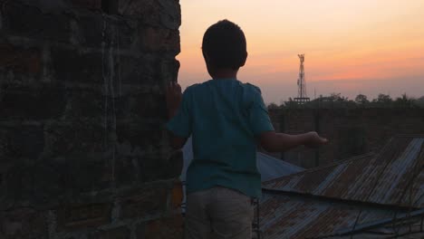 Niño-Arrojando-Piedras-Desde-La-Azotea-En-Sylhet-Durante-La-Puesta-De-Sol,-Bangladesh