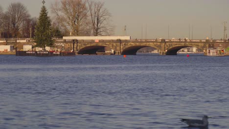 View-of-Lombardsbrücke-Bridge-in-Hamburg,-Germany,across-Inner-Alster-Lake-with-a-train-moving-across-and-a-Christmas-tree-in-the-foreground