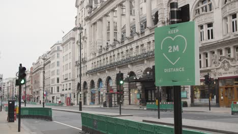 Lockdown-in-London,-slow-motion-pan-of-COVID-19-2020-pandemic-KEEP-2M-DISTANCE-sign-on-empty-Piccadilly-streets,-with-flying-birds-and-lone-people