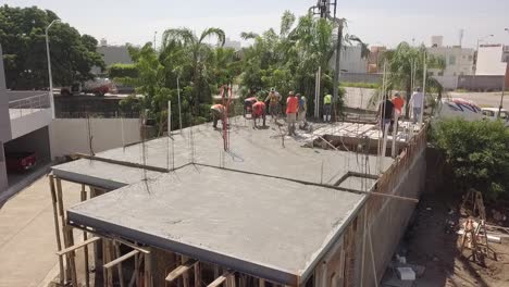 Aerial-above-roof-pouring-cement-to-build-roof-or-floor-structure-wearing-orange-vests-as-construction-workers-working-on-site