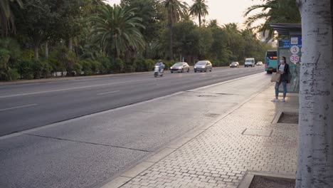 Frau-Wartet-An-Der-Bushaltestelle-Auf-Belebten-Straßen-Von-Malaga,-Spanien