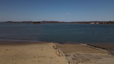 Drone-flying-quickly-over-beach-signage-and-a-boat-ramp-on-the-way-to-buoys-on-the-deep-blue-Hingham-Harbor