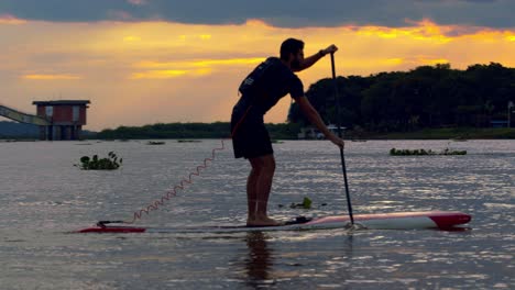 Ein-Mann-Steigt-Während-Eines-Atemberaubenden-Sonnenuntergangs-Auf-Ein-Paddelbrett-Am-Rio-Paraguay