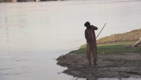 Retrato-Ambiental,-Un-Hombre-Pakistaní-Arroja-Barro-A-Un-Río-Con-Un-Bastón