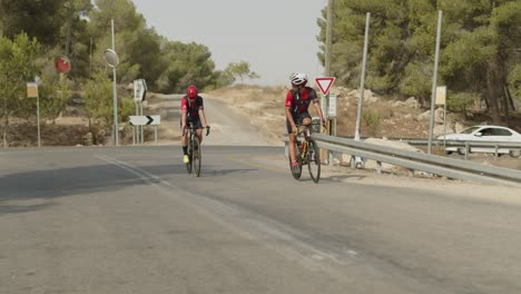 Zwei-Profi-Radfahrer-In-Zeitlupe-Fahren-Auf-Der-Leeren-Straße-Im-Wald-Und-Bitten-Die-Fahrer-Hinter-Ihnen-Um-Entschuldigung