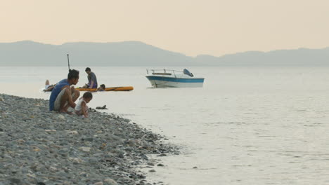 Langsame-Zeitlupenaufnahme-Des-Vaters-Und-Seiner-Kleinen-Tochter,-Die-Steine-An-Einen-Felsigen-Strand-In-Asien-Werfen