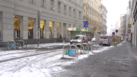 Paisaje-Urbano-Típico-De-La-Ciudad-Con-Coches-Conduciendo-Y-Gente-Caminando-Con-Mucha-Nieve