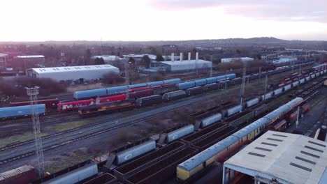 Vista-Aérea-Del-Amanecer-De-Largas-Vías-De-Ferrocarril-Con-Vagones-De-Locomotoras-Diésel-Pesados-Y-Toma-De-Distancia-Del-Patio-De-Contenedores-De-Carga