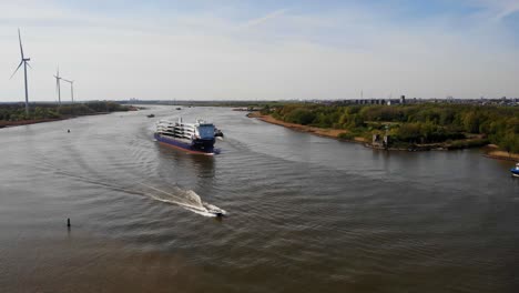 Vista-Aérea-Del-Buque-De-Carga-Del-Proveedor-De-La-Sinfonía-Que-Se-Acerca-A-La-Curva-Del-Río-En-Oude-Maas-En-Barendrecht-Con-Lancha-Rápida-Pasando