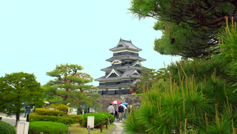 Matsumoto,-Nagano,-Ca.-Mai-2022:-Touristen-Schlendern-An-Einem-Regnerischen-Frühlingstag-Mit-Bunten-Sonnenschirmen-Durch-Den-Japanischen-Garten-Der-Majestätischen-Burg-Matsumoto-Durch-Eine-Prächtige-Kiefer