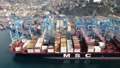 Aerial-truck-right-of-a-container-cargo-ship-docked-near-cranes-ready-to-be-loaded-in-Valparaiso-Sea-Port,-Chile