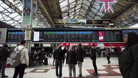 Vista-Interior-De-Los-Viajeros-Mirando-El-Tablero-De-Salida-En-La-Estación-De-Tren-Victoria-En-Londres-El-12-De-Abril-De-2022