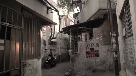 Sudeste-Asiático-Con-Moto-Conduciendo-En-Un-Callejón-Y-Una-Persona-Sentada-En-Una-Moto,-En-Algún-Lugar-De-Yakarta