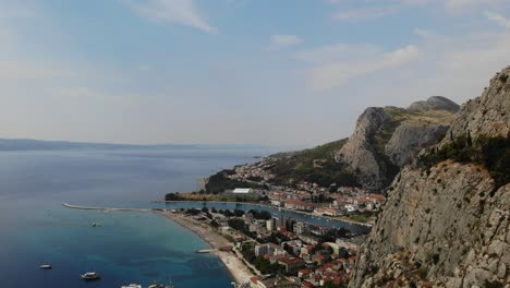 Imágenes-De-Aproximación-Aérea-De-Un-Día-Soleado-De-Verano-Sobre-La-Ciudad-De-Omis,-El-Río-Cetina-Y-Los-Acantilados