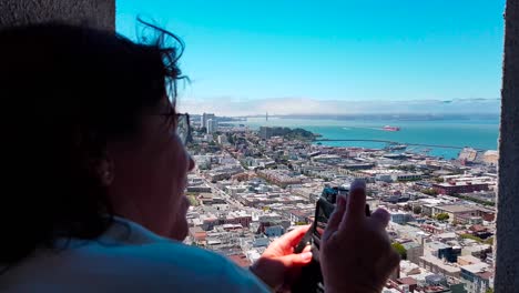 Mujer-Tomando-Una-Foto-De-La-Bahía-De-Sf-Desde-La-Parte-Superior-De-La-Torre-Coit-Con-Vistas-A-San-Francisco,-California,-Ee.uu.