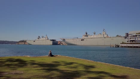 A-female-professional-office-worker-sits-by-the-wharf-enjoying-the-view-of-two-warships-and-harbour-during-her-lunch-break-on-a-sunny-day