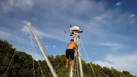 Hombre-Escalando-El-Mástil-Del-Velero-Trimarán-Bigkanu-En-Un-Lugar-De-Arrecife-De-Coral,-Tiro-De-Elevación-De-Pedestal-Aéreo