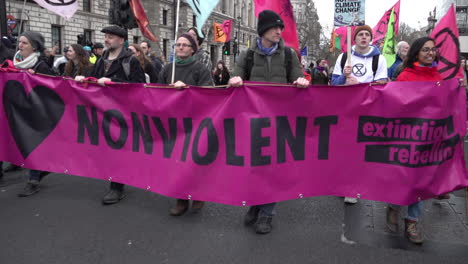 Los-Manifestantes-Del-Cambio-Climático-De-La-Rebelión-De-Extinción-Marchan-Con-Una-Gran-Pancarta-Rosa-Brillante-Que-Dice-&quot;no-Violento&quot;