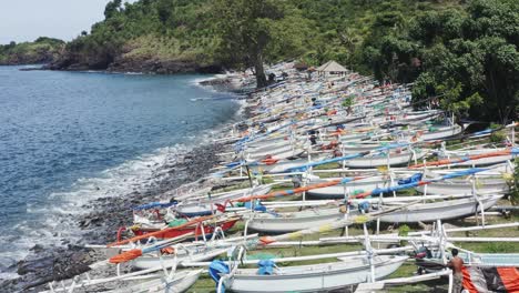 Barcos-De-Pesca-Jukung-Alineados-En-La-Playa-De-Amed-Mientras-Los-Pescadores-Los-Reparan,-Vista-Aérea-Del-Sobrevuelo