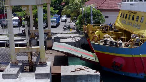 Nusa-Jaya-Abadi-vehicle-and-passenger-ferry-at-Port-Roro-lowering-ramp,-Aerial-side-view-hover-shot