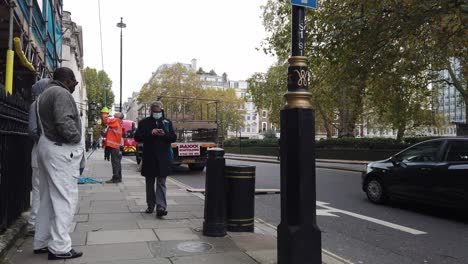 Two-workers-talking-people-walking-along-road-one-man-wearing-a-mask-October-2020