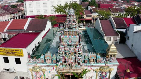 Enfoque-Aéreo-Del-Templo-Hindú-Sri-Mariamman-Con-Banderas-De-Oración-Y-Fachada-De-Deidad-Elaborada,-Toma-De-Drones