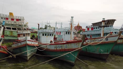 Fishing-Boats-moored-in-the-mud-at-a-river-bank-during-the-low-tide-in-Samut-Sakhon,-Thailand-and-waiting-to-be-deployed-again