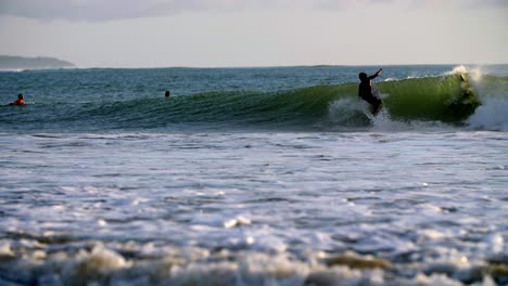 Native-surfer-catching-and-riding-a-large-wave-in-front-of-other-surfers-in-slow-motion,-left-tracking-shot