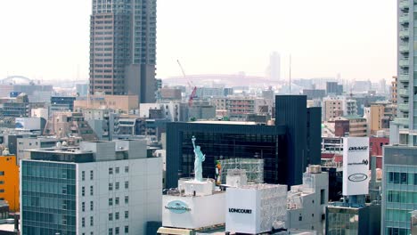 Vista-De-Un-Lugar-Comercial-En-La-Ciudad-Con-Una-Réplica-De-La-Estatua-De-La-Libertad-En-La-Azotea-Del-Centro-Comercial-De-Entretenimiento-Amerikamura,-Tiro-Alto-Bloqueado