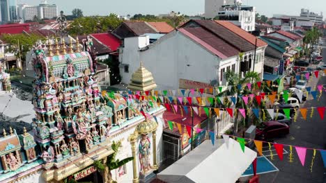 Sri-Mariamman-Hindu-Tempel-Mit-Ausgestreckten-Gebetsfahnen-Und-Fliegenden-Amseln-Am-Ende,-Drohnen-Umlaufaufnahme-Aus-Der-Luft